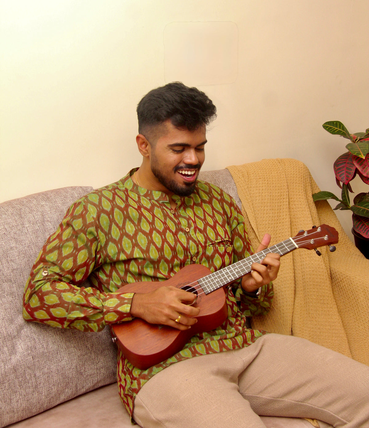 Aam Panna olive green Sambalpuri ikat handloom kurta for men, seated with a ukulele